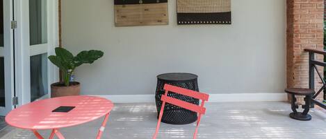 A small patio area with a red table and chair, a potted plant, and two wall-mounted decorative panels.