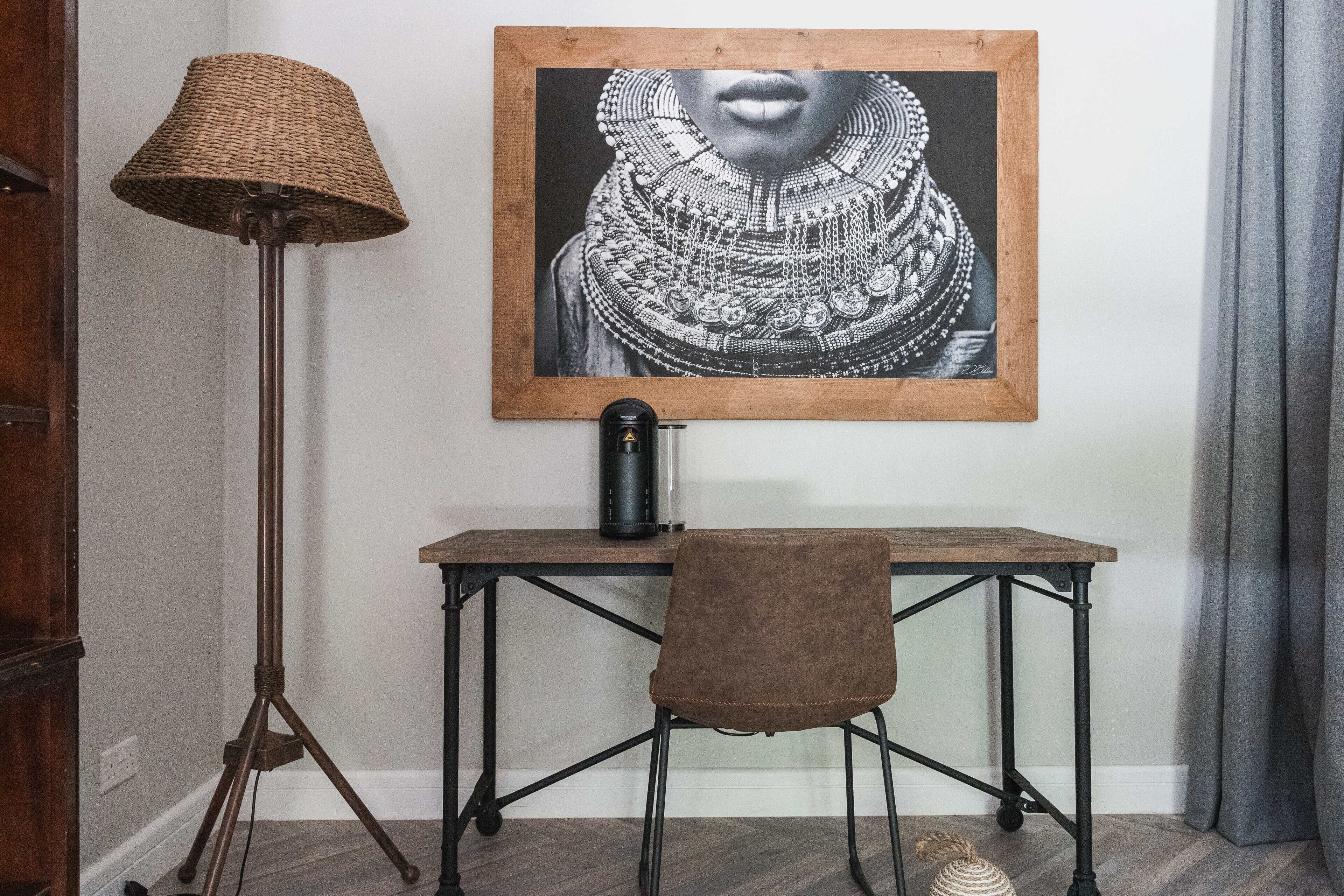 A room with a wooden desk, a brown chair, a floor lamp, and a framed artwork on the wall.