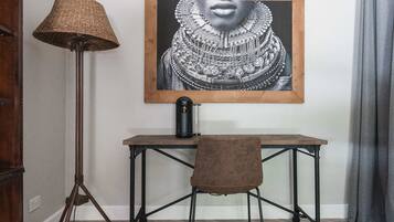 Una habitación con un escritorio de madera, una silla marrón, una lámpara de pie y una obra de arte enmarcada en la pared.