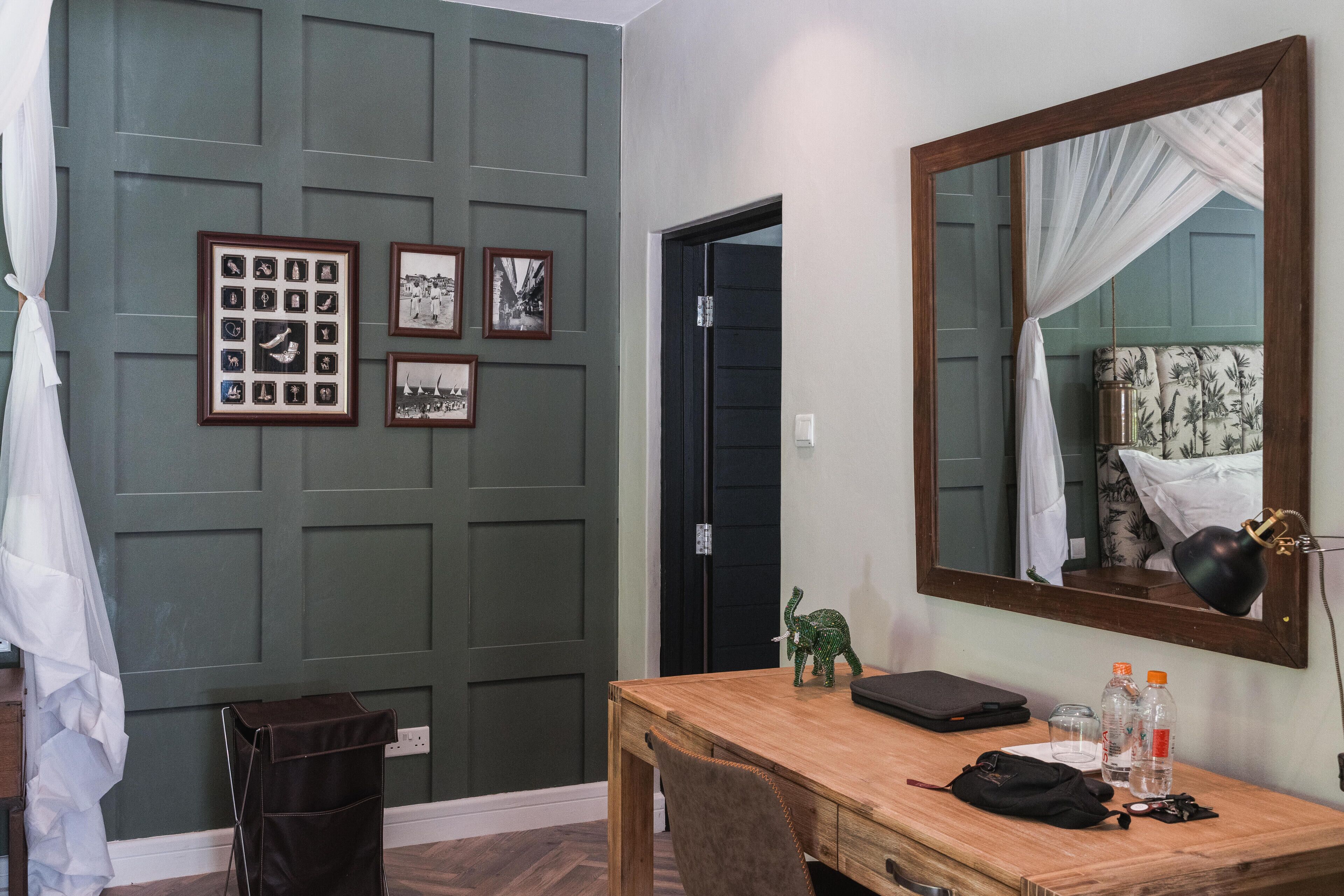 Una habitación con un escritorio de madera, un espejo, cuadros en la pared y una puerta negra.