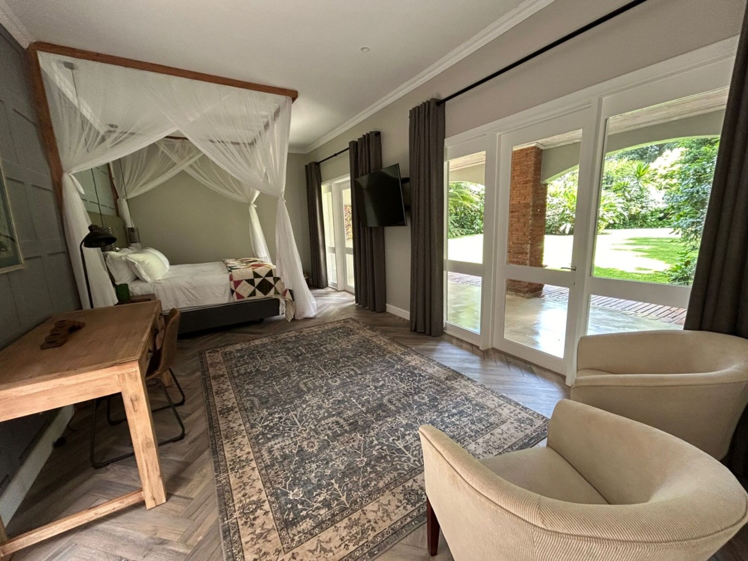 A bedroom with a canopy bed, a desk, a chair, a large rug, and a TV mounted on the wall.