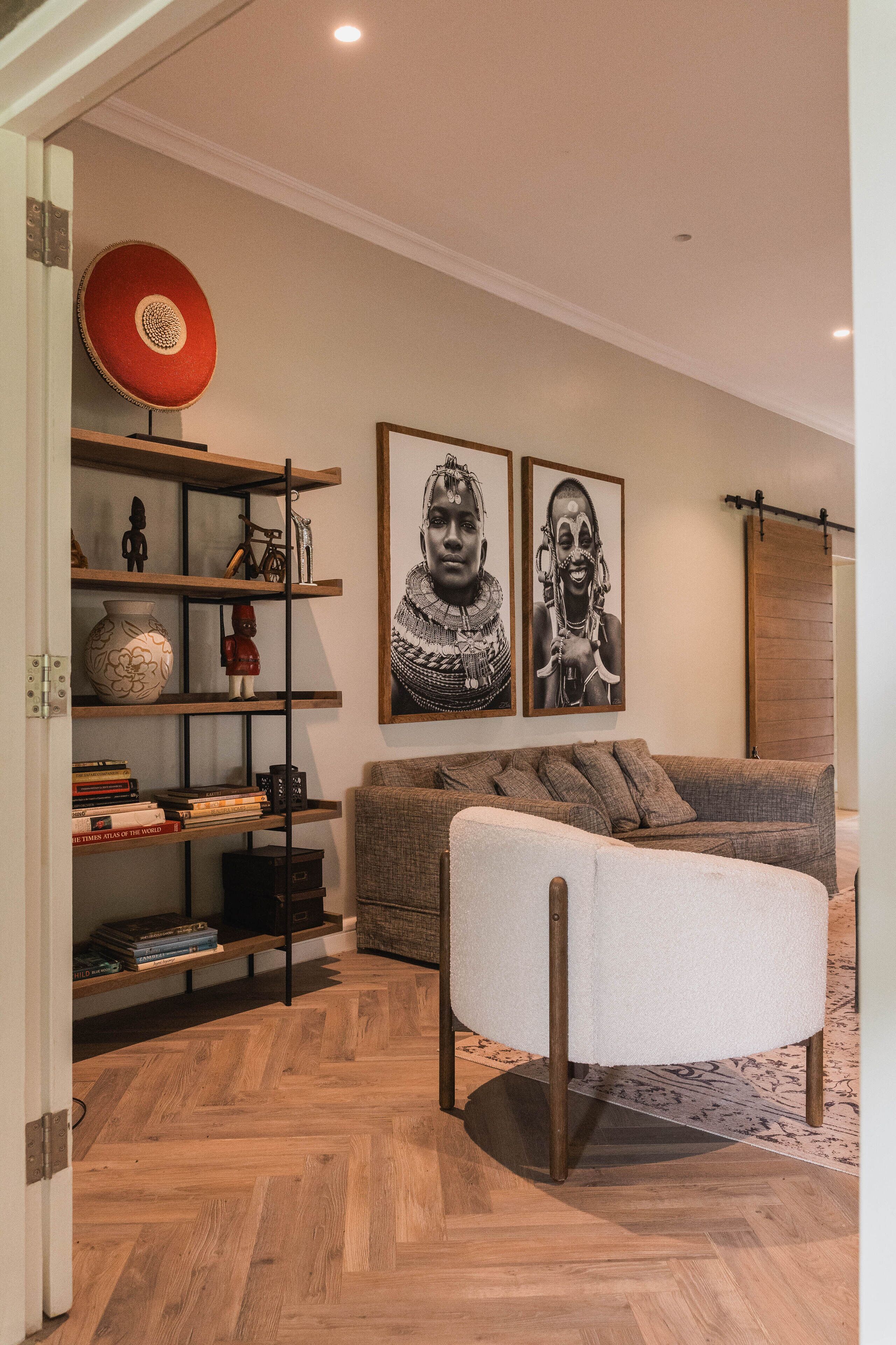 Un salon doté d’un parquet en bois à motifs chevrons, d’un canapé gris, d’un pouf blanc et d’une bibliothèque agrémentée de divers objets décoratifs.