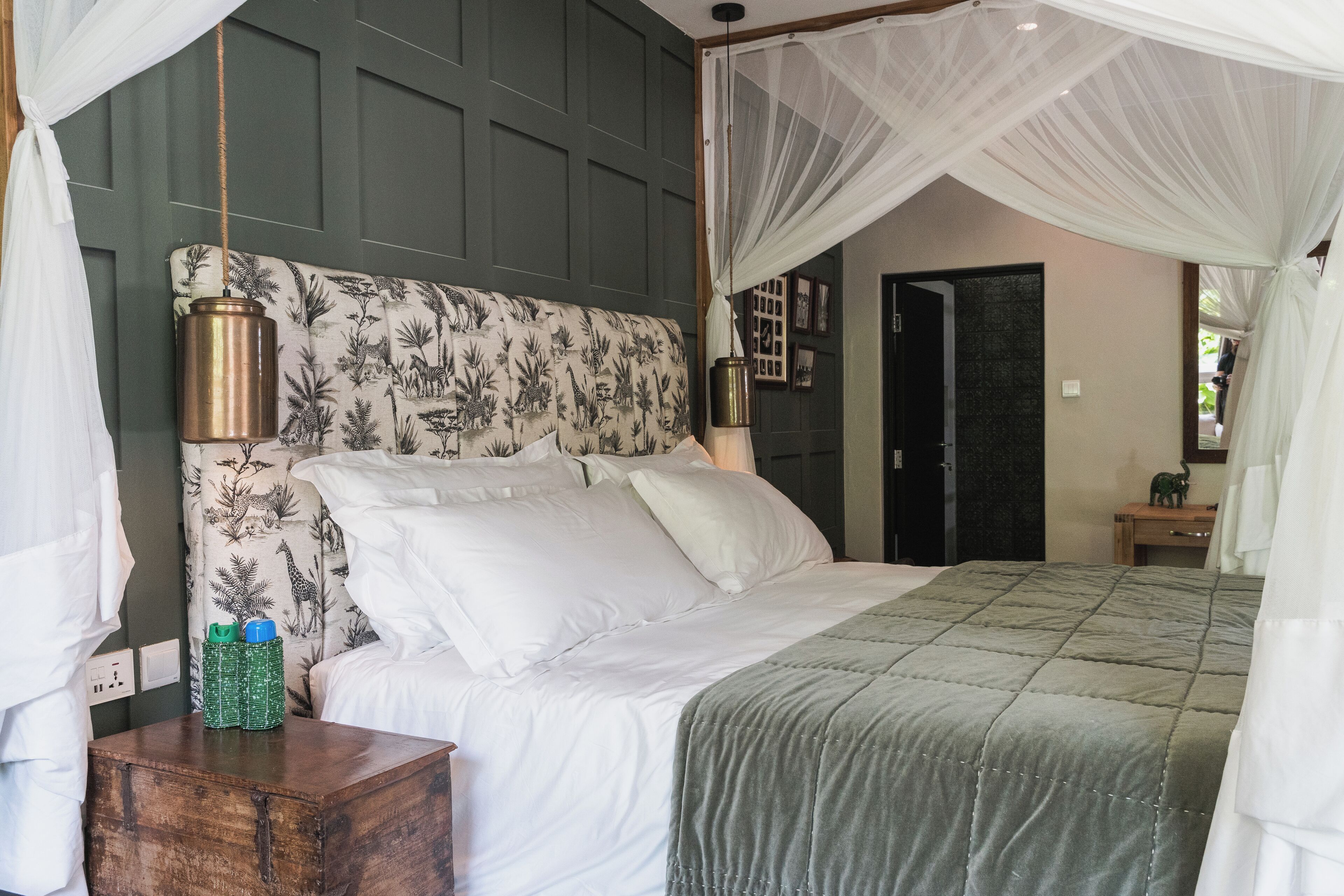 A bedroom with a canopy bed, a bedside table with bottles, and a green headboard.