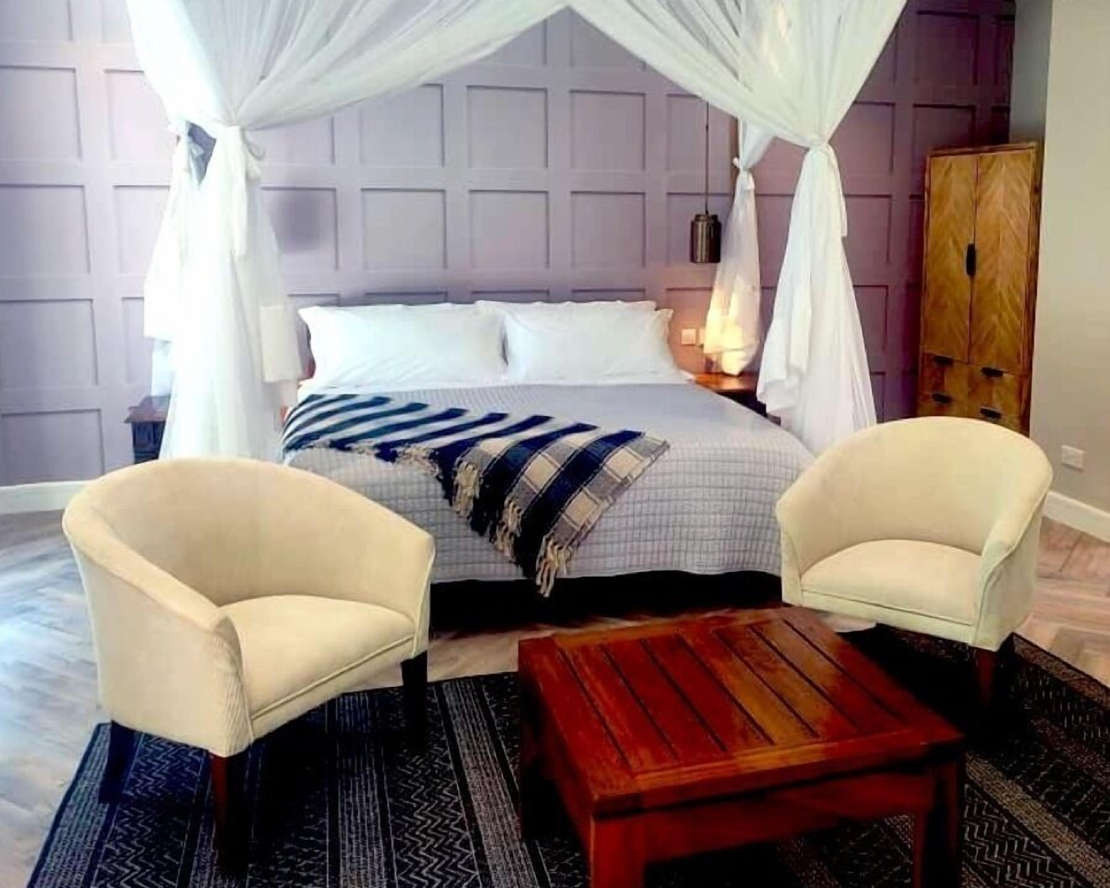 A bedroom with a bed, two armchairs, a nightstand, a wooden table, and a wardrobe.
