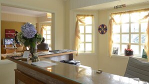 Un área de recepción con un mostrador de vidrio, un jarrón con flores, un cartel de bienvenida y un dardo en la pared.