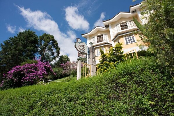 A large, multi-story building with a traditional architectural style, surrounded by lush greenery and flowering plants.