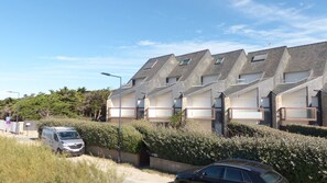 A row of modern, two-story houses with sloped roofs and large windows, surrounded by dense shrubbery.