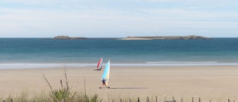A sandy beach with a wooden fence in the foreground and a clear view of the sea and distant islands.
