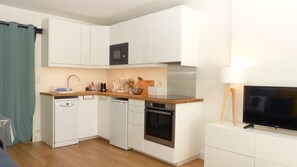 A compact kitchen with white cabinets, a microwave, a stove, and a dishwasher. There is a wooden countertop, a sink, and a television on a stand. - Waterfront studio in Penthièvre (Saint-Pierre-Quiberon)