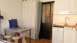 Eine kleine Küche mit Spüle, einer Arbeitsfläche und einem Kühlschrank. Ein Tisch mit zwei Stühlen und einem Laptop sind ebenfalls vorhanden.