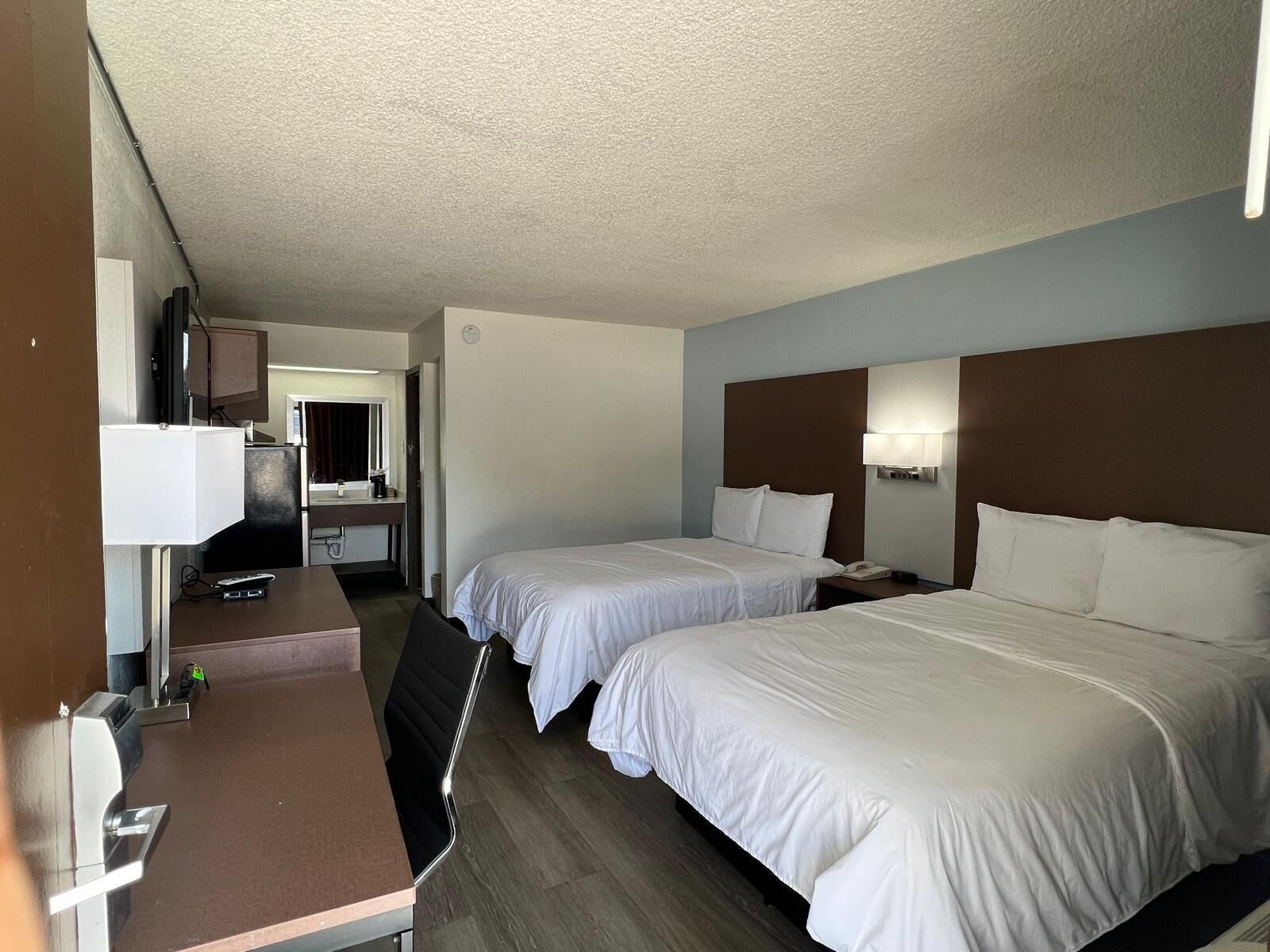 Een hotelkamer met twee bedden, een bureau, een stoel, een kleintje tafeltje, een lamp en een spiegel.
