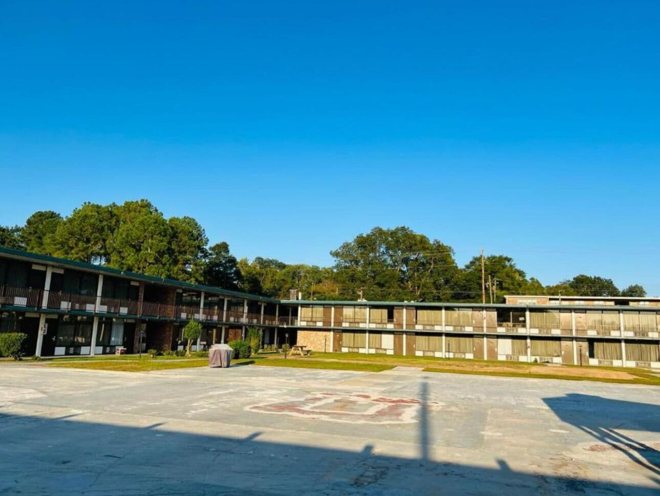 A large, multi-story building with a flat roof, surrounded by a parking lot and trees.