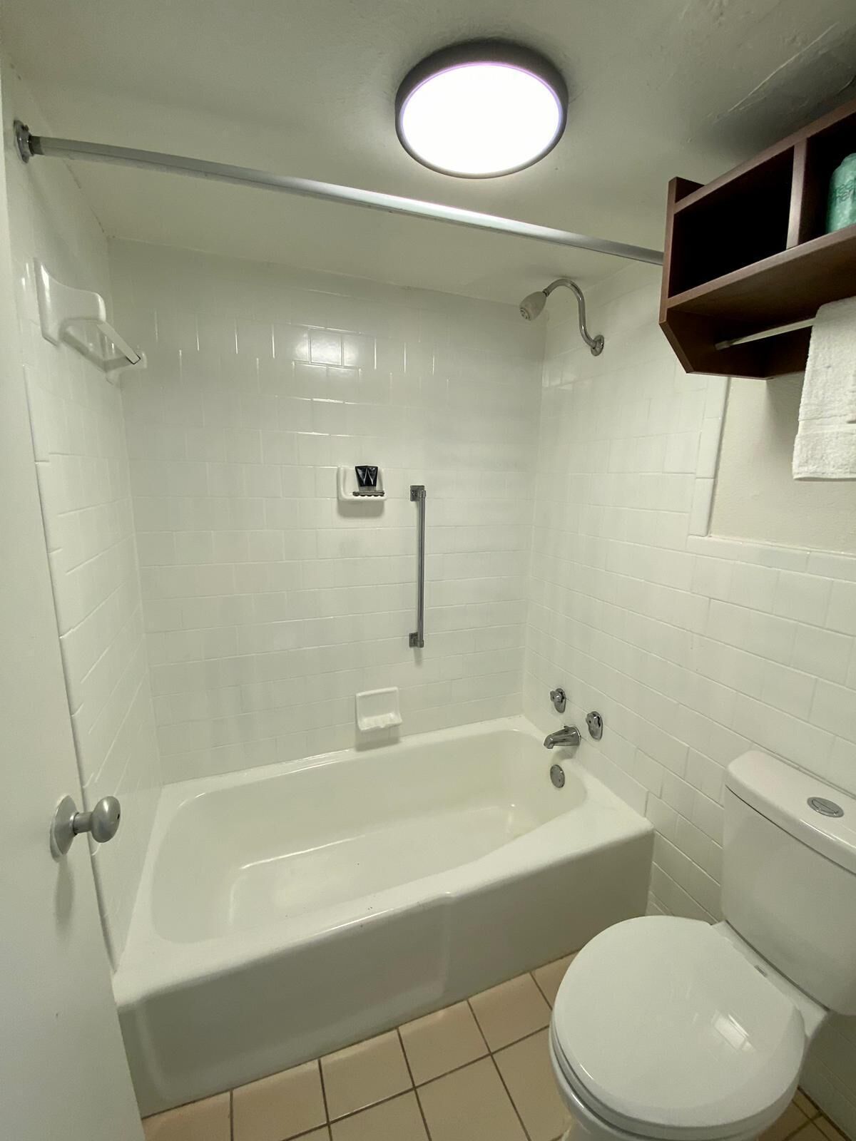A bathroom with a bathtub, toilet, and a shelf with a towel.