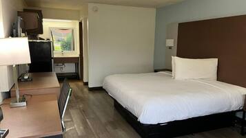 Habitación de hotel con cama, escritorio, silla, televisión y ventana.