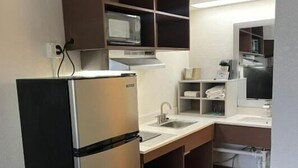 Eine kompakte Küche mit integriertem Mikrowellenherd, einem Edelstahlkühlschrank und Holzschränken.