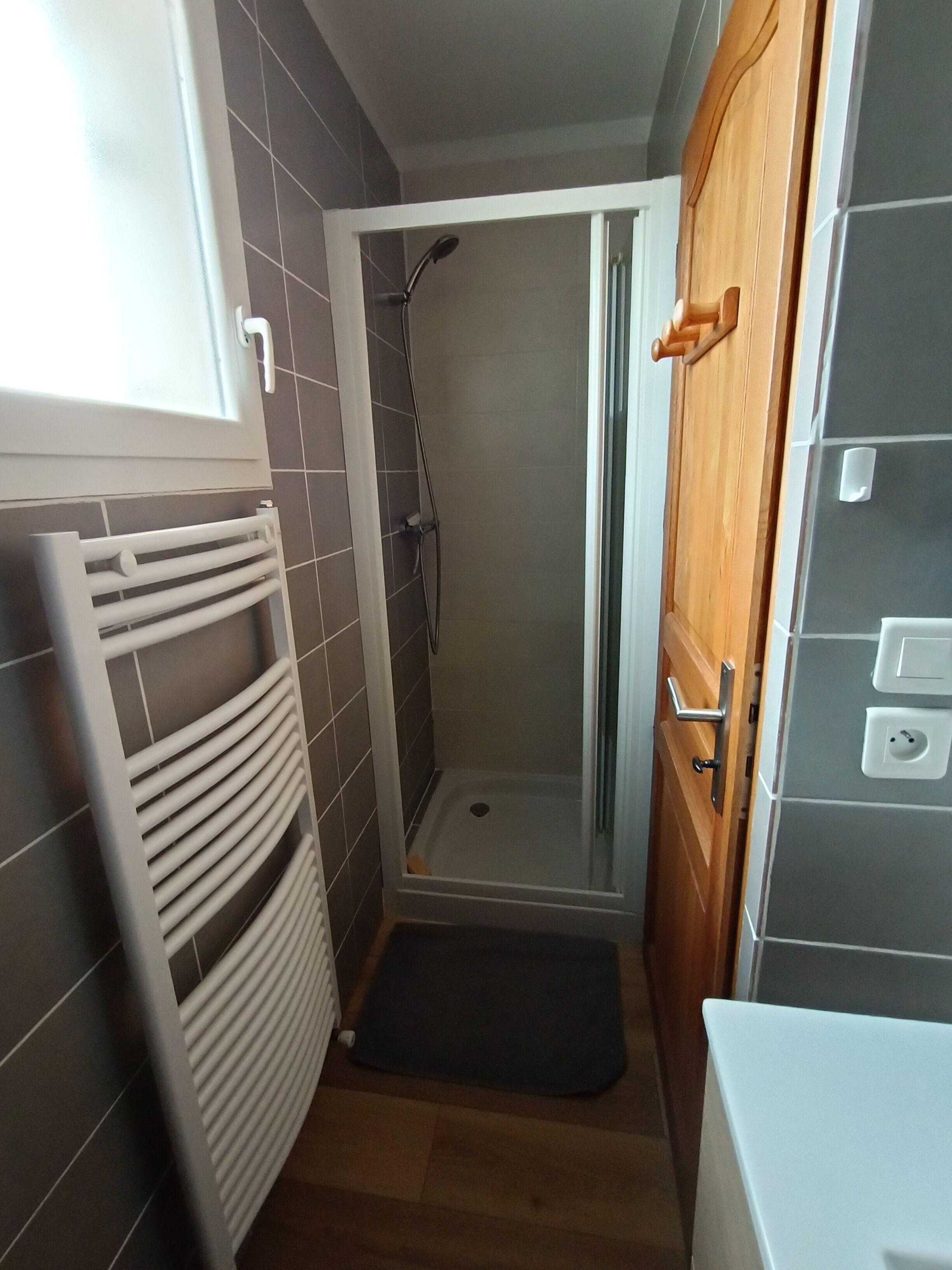 Ein kleines Badezimmer mit Dusche, einem weißen Heizkörper und einer Holztür.