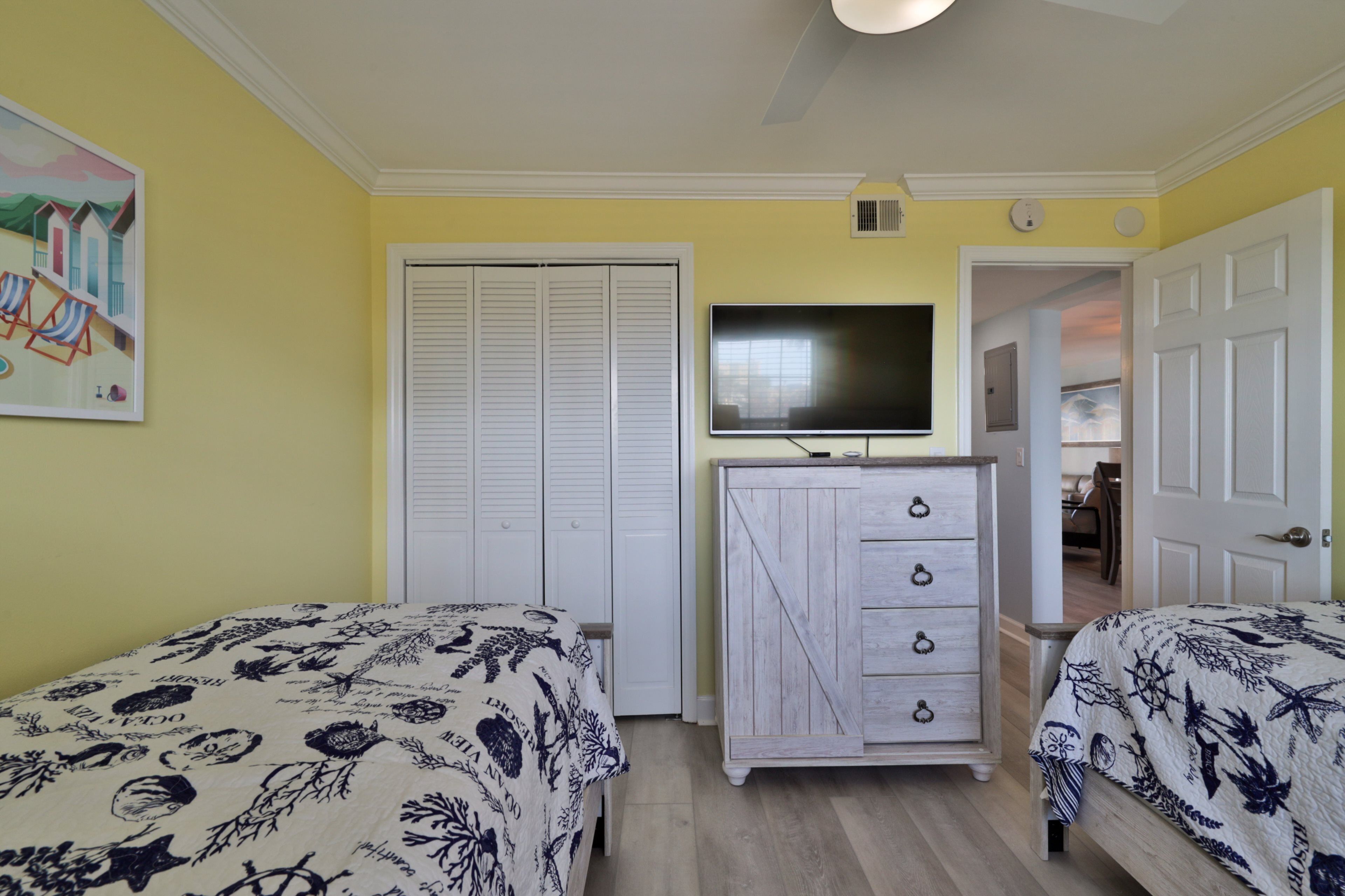 A bedroom with two beds, a TV mounted on the wall, and a wardrobe.
