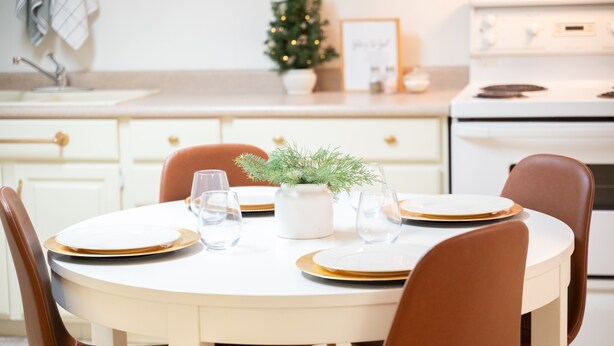 Een ronde eettafel met witte borden en gouden randen, omringd door bruine stoelen.