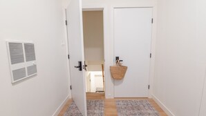 Een hal met twee witte deuren, een witte ventilatieopening in de linker muur en een geweven mand aan de rechterdeur.