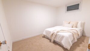 Een slaapkamer met een enkel bed, een beigekleurig tapijt, witte muren en een klein raam.