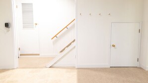 Een kamer met een witte deur, een houten trap en een witte muur.