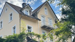 En toetagers bolig med balkon på anden sal, omgivet af grønt.