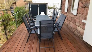 En træterrasse med et bord og stole, en hængestol og en murstensvæg.