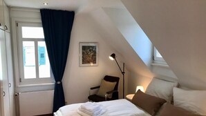 Et soveværelse med seng, stol, skrivebord og et vindue med gardiner.