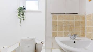 Une salle de bain avec des toilettes, un lavabo et une fenêtre agrémentée d’une plante.