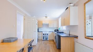 A compact kitchen with a dining area, a built-in oven, and a refrigerator. - Spacious 3BDR Kennington Home with Private Garden (London)