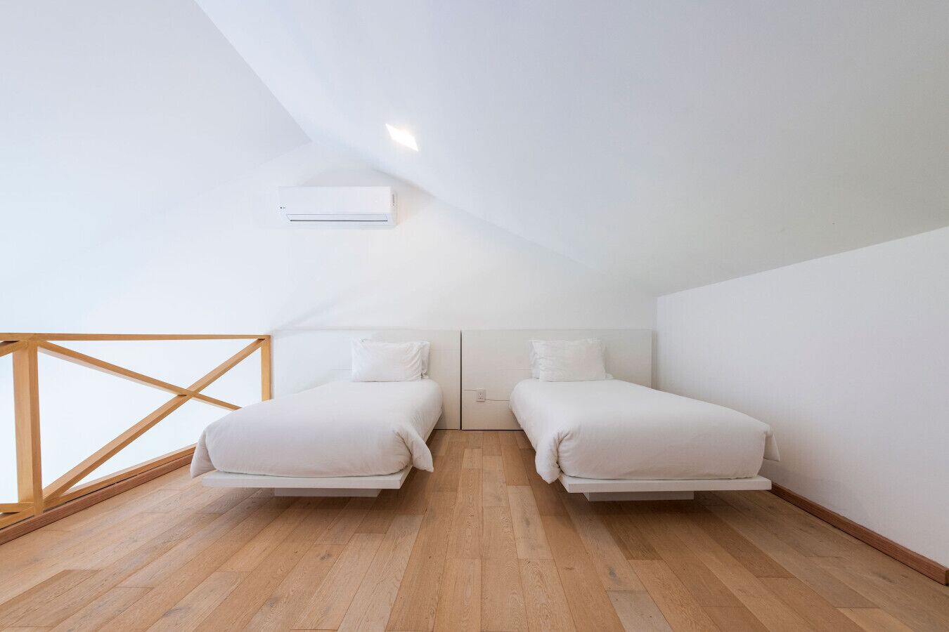 Un dormitorio pequeño y moderno con dos camas, suelo de madera y techo inclinado.
