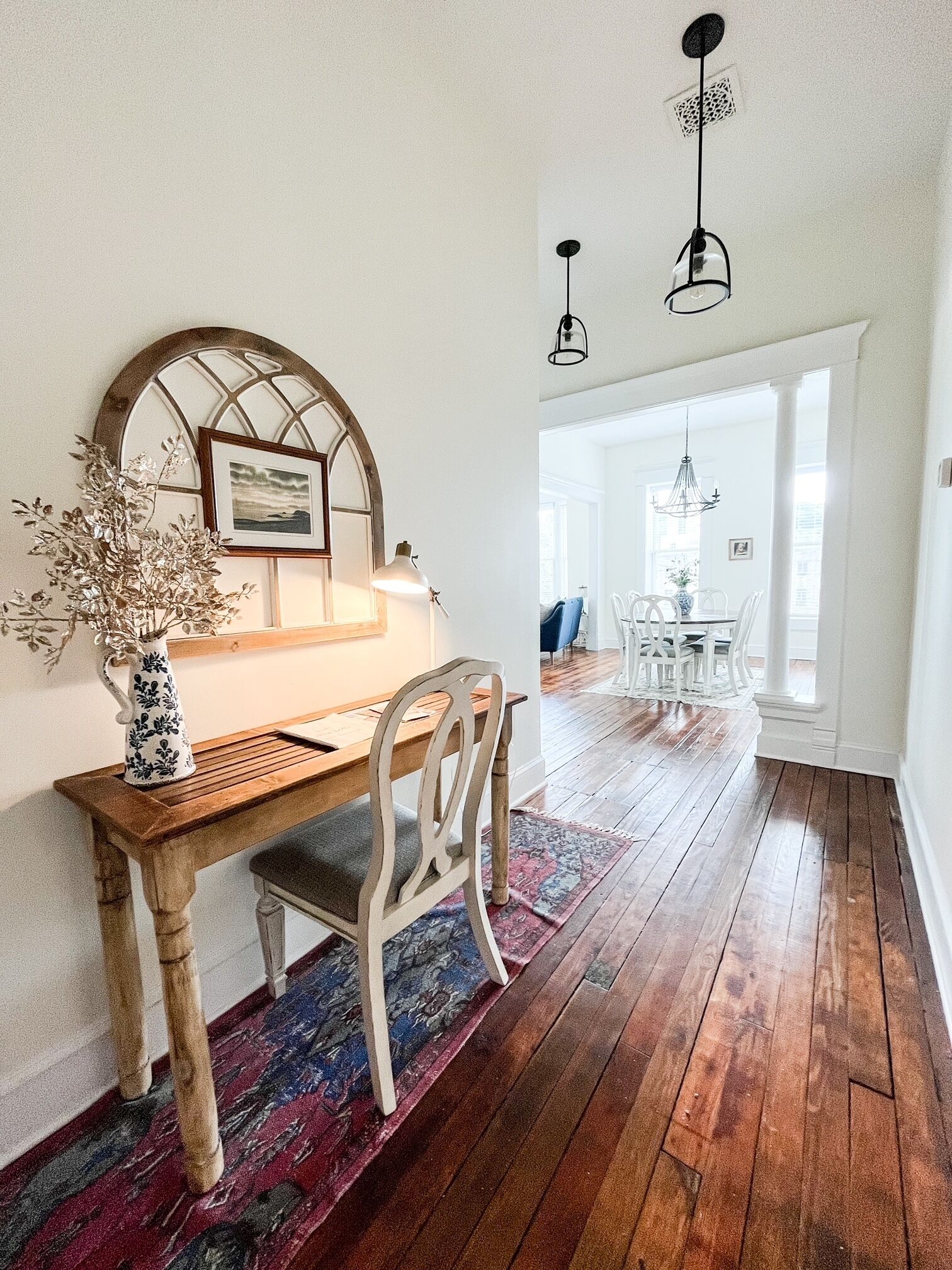 Un coin repas avec une table en bois, des chaises blanches, un tapis à motifs et un luminaire suspendu.