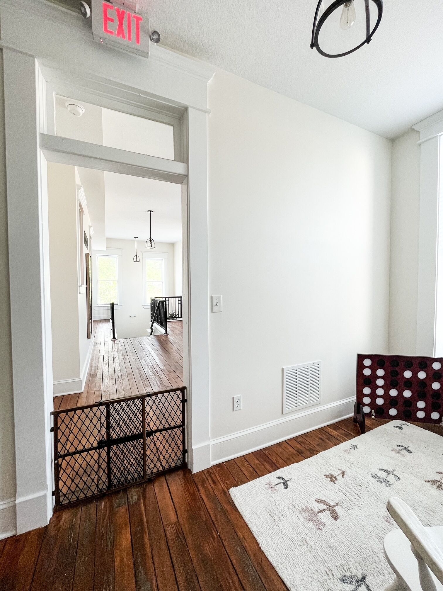 A spacious room with a wooden floor, white walls, and a visible exit sign.