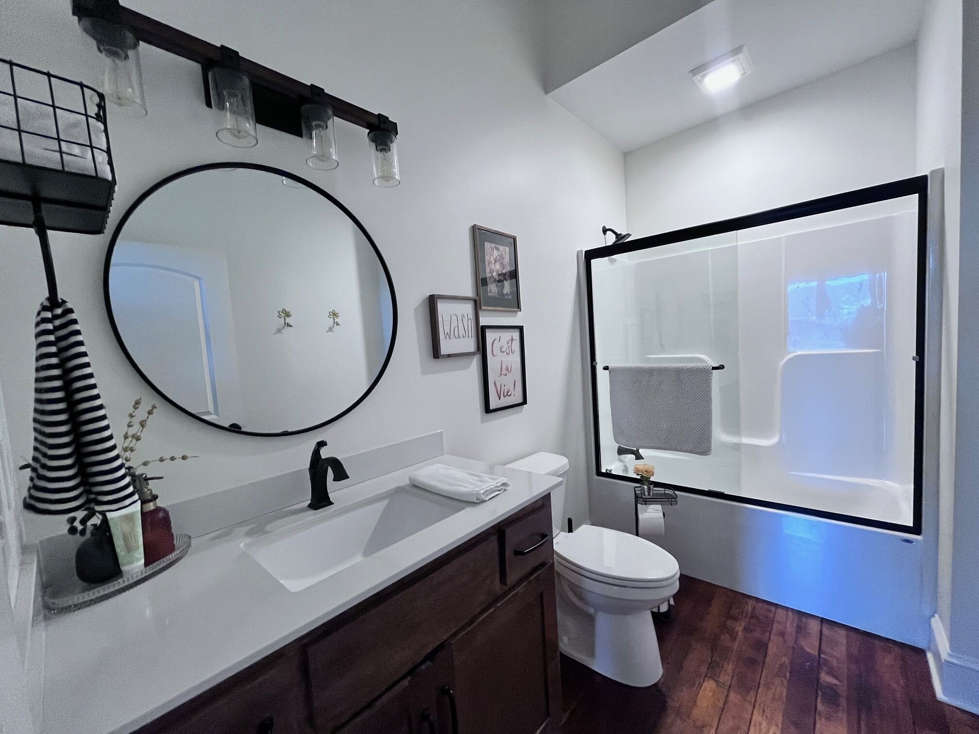 A modern bathroom with a large mirror, a white sink, a toilet, and a shower area.