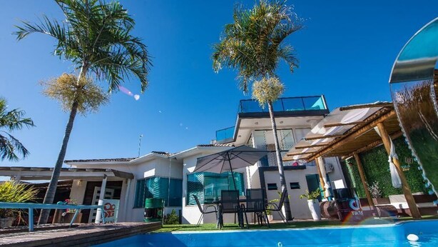 A modern house with a swimming pool, surrounded by palm trees and a clear blue sky. - Quarto Spotify (Taguatinga)
