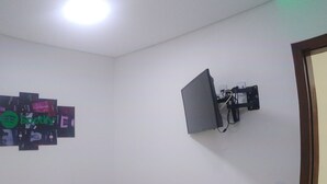 A bedroom with a bed, a wall-mounted TV, and a ceiling light. - Quarto Spotify (Taguatinga)