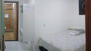A small, clean room with a bed, a wooden door, and a white wall. - Quarto Spotify (Taguatinga)