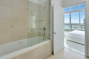 A modern bathroom with a glass-enclosed shower, a white bathtub, and a balcony with a bed. - 28th Floor Icon Brickell Oasis with City Views (Miami)