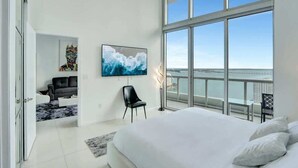 Une chambre moderne avec un grand lit, un téléviseur fixé au mur et un balcon offrant une vue sur la mer.
