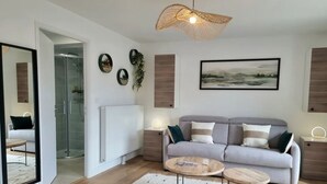 Un salon moderne avec un canapé gris, deux tables d’appoint, une table basse et une cabine de douche en verre.