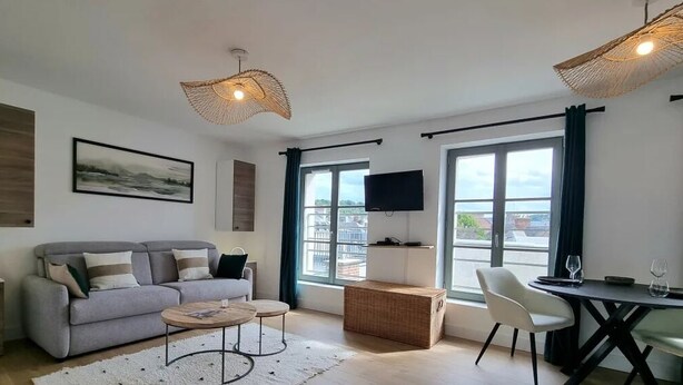 Un salon moderne avec un canapé, une table basse et une table à manger. Un téléviseur est fixé au mur et il y a une fenêtre avec des rideaux.