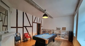 A room with a pool table, a red chair, and a bookshelf.