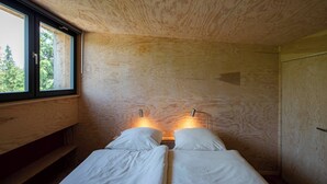 Een kamer met twee bedden, houten wanden, een raam en een deur.