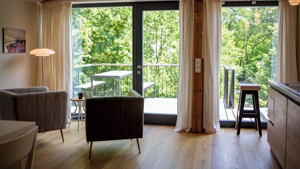 Een moderne kamer met een grote schuifglazen deur naar een balkon, een eethoek en een zithoek met een lamp.