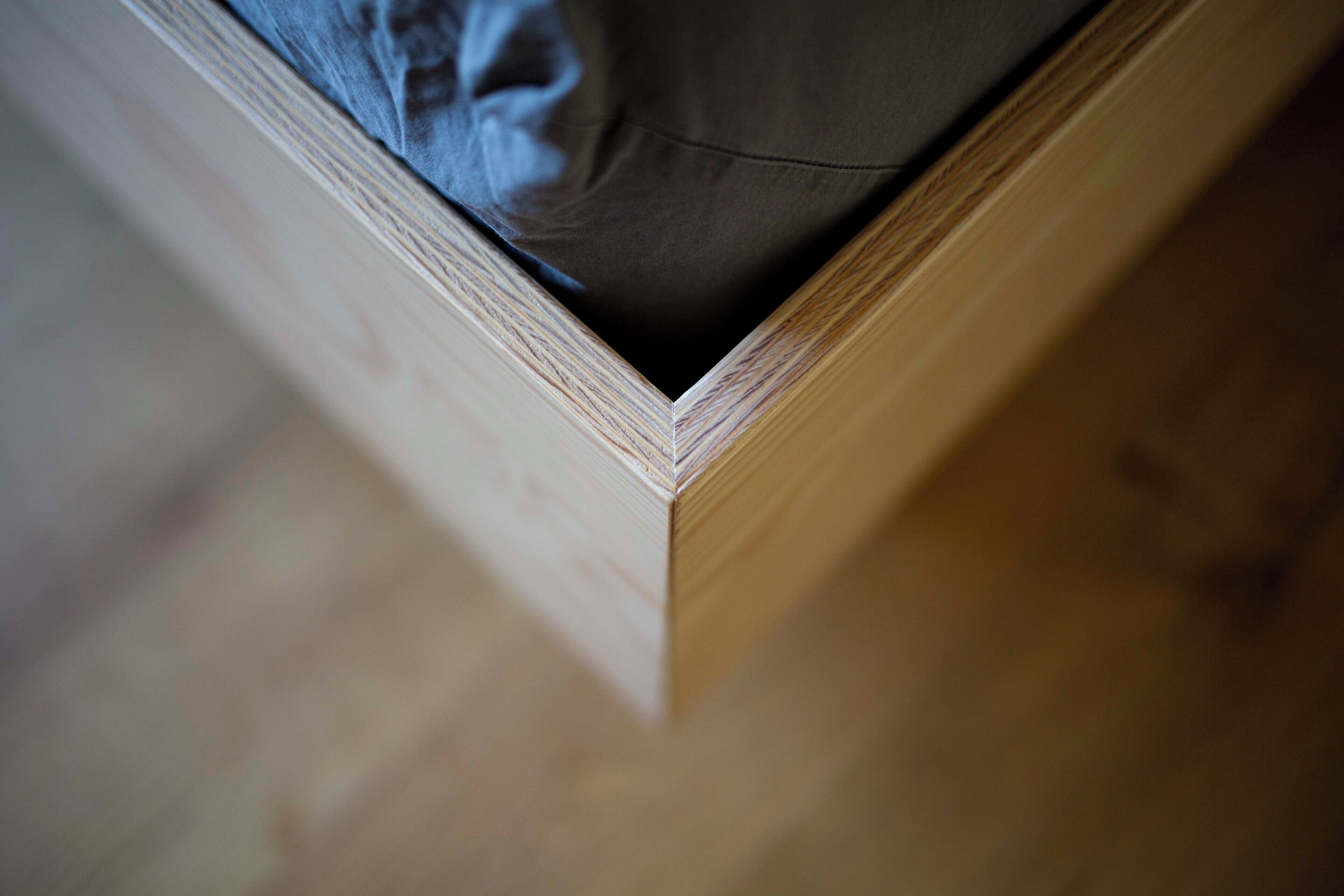 Un coin d’un cadre de lit en bois, avec un matelas visible à l’intérieur.