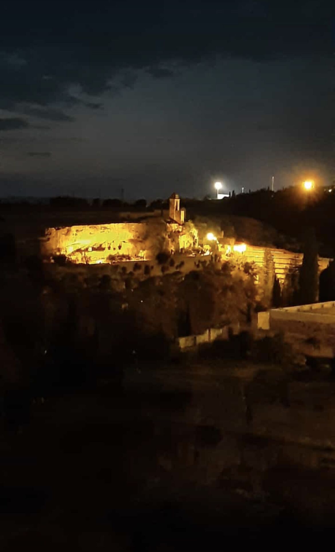 Sítio histórico à noite, com estruturas e ruínas iluminadas.