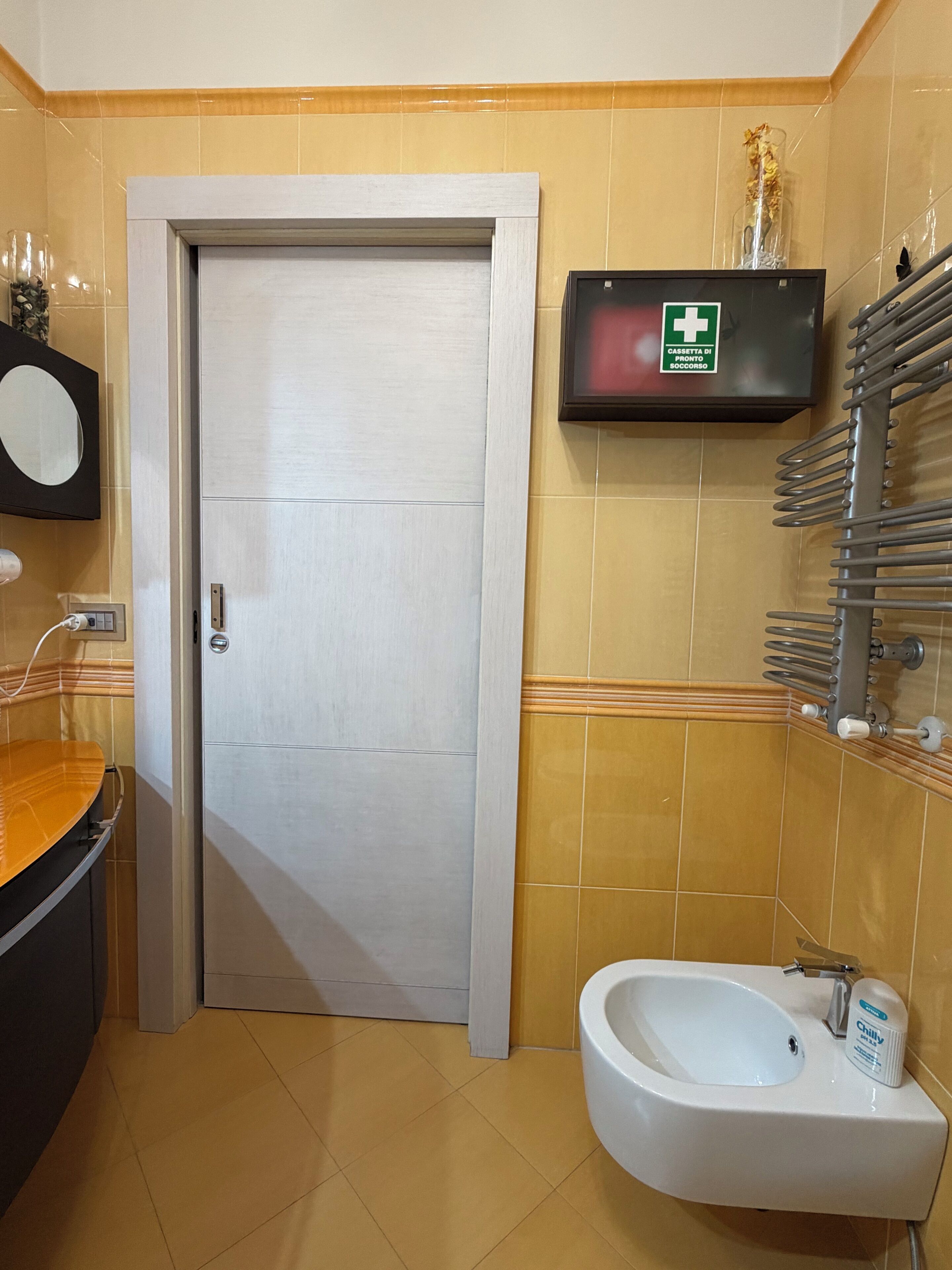 A bathroom with a white sink, a bidet, a mirror, and a wall-mounted TV.
