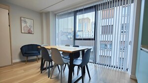 Ein modernes Zimmer mit einem Holzesstisch, vier Stühlen, einem blauen Sofa und einem großen Fenster mit Jalousien.