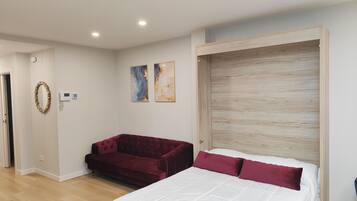 A bedroom with a bed, a red sofa, a wooden headboard, and two abstract paintings on the wall.