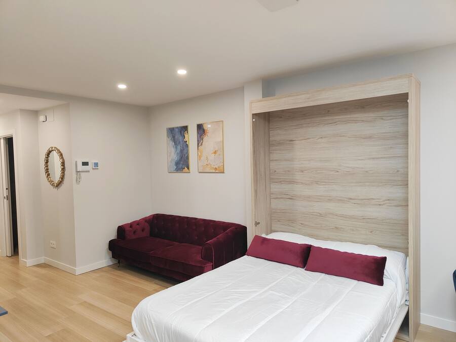 A bedroom with a bed, a red sofa, a wooden headboard, and two abstract paintings on the wall.